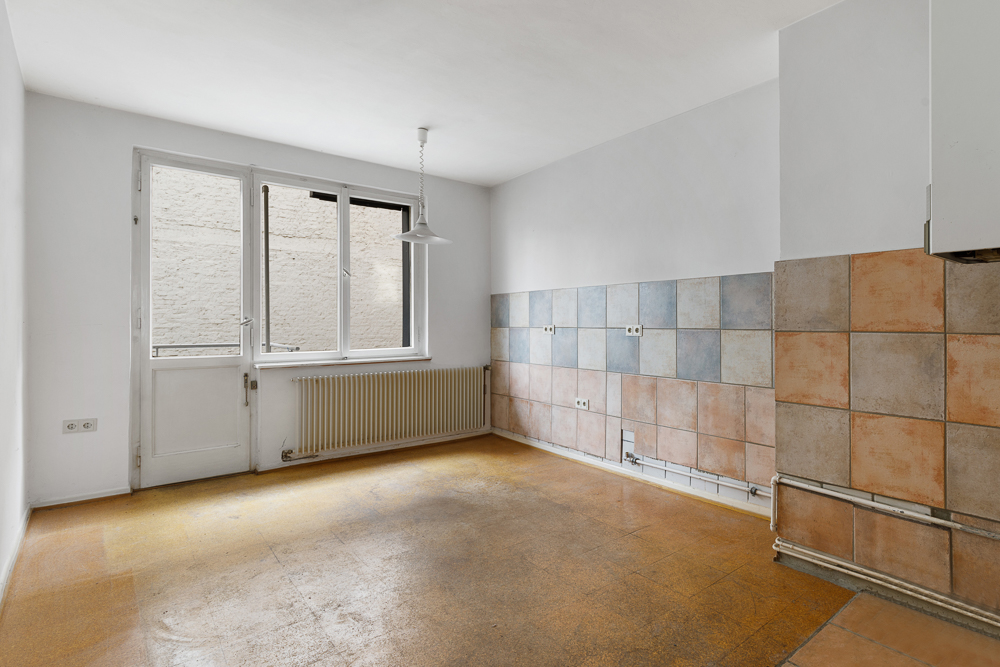Leerer Raum mit gefliestem Bereich, Fenster, Tür und Heizkörper, Lampenhängevorrichtung an der Decke.