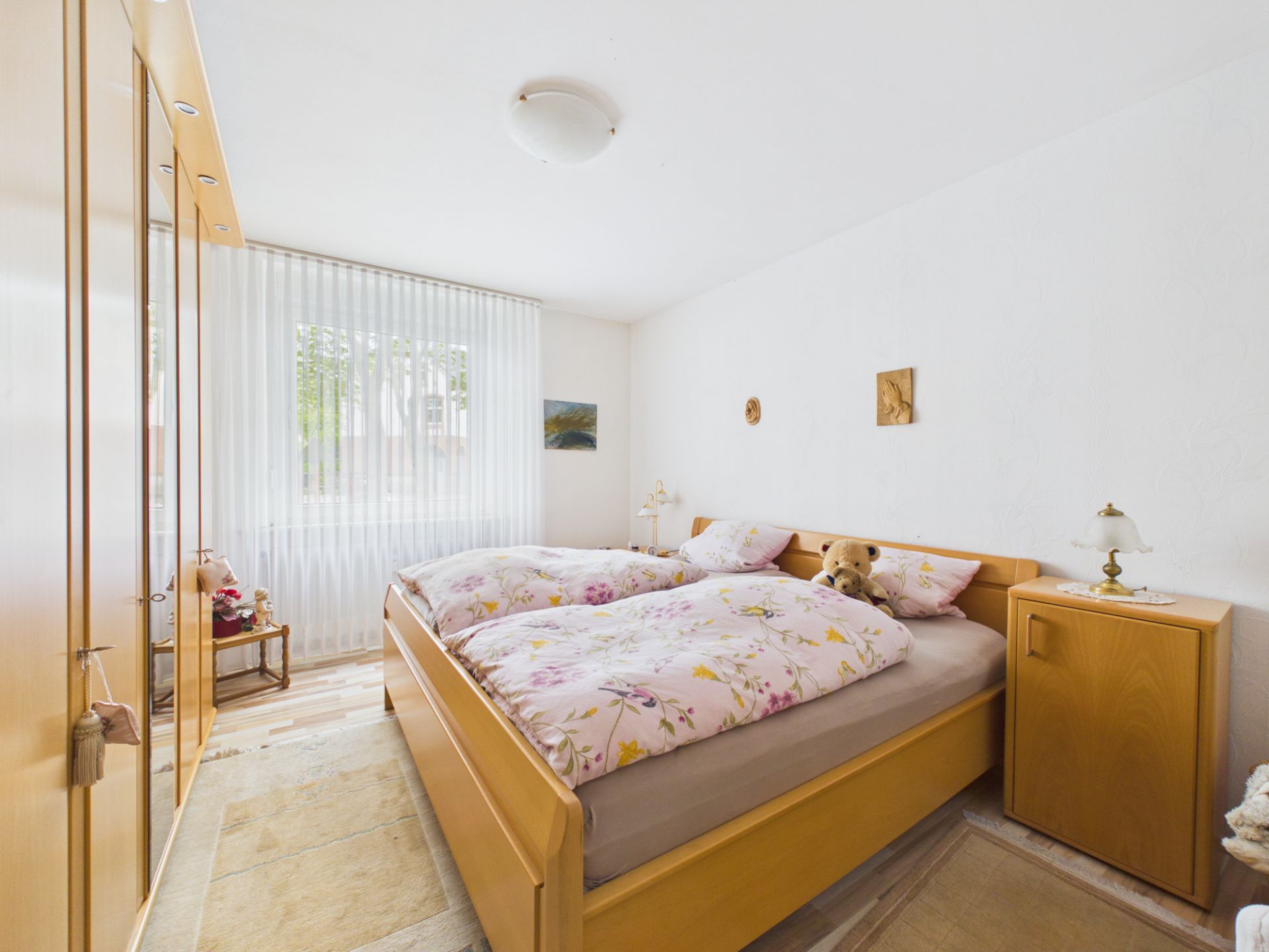 Helles Schlafzimmer mit Doppelbett, Holzschrank, Fenster und Nachttischen.