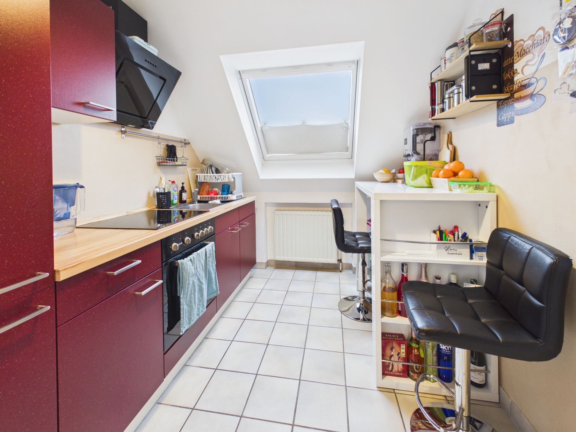Moderne Küche mit roten Schränken, Fenster, Tresen und zwei schwarzen Barhockern.