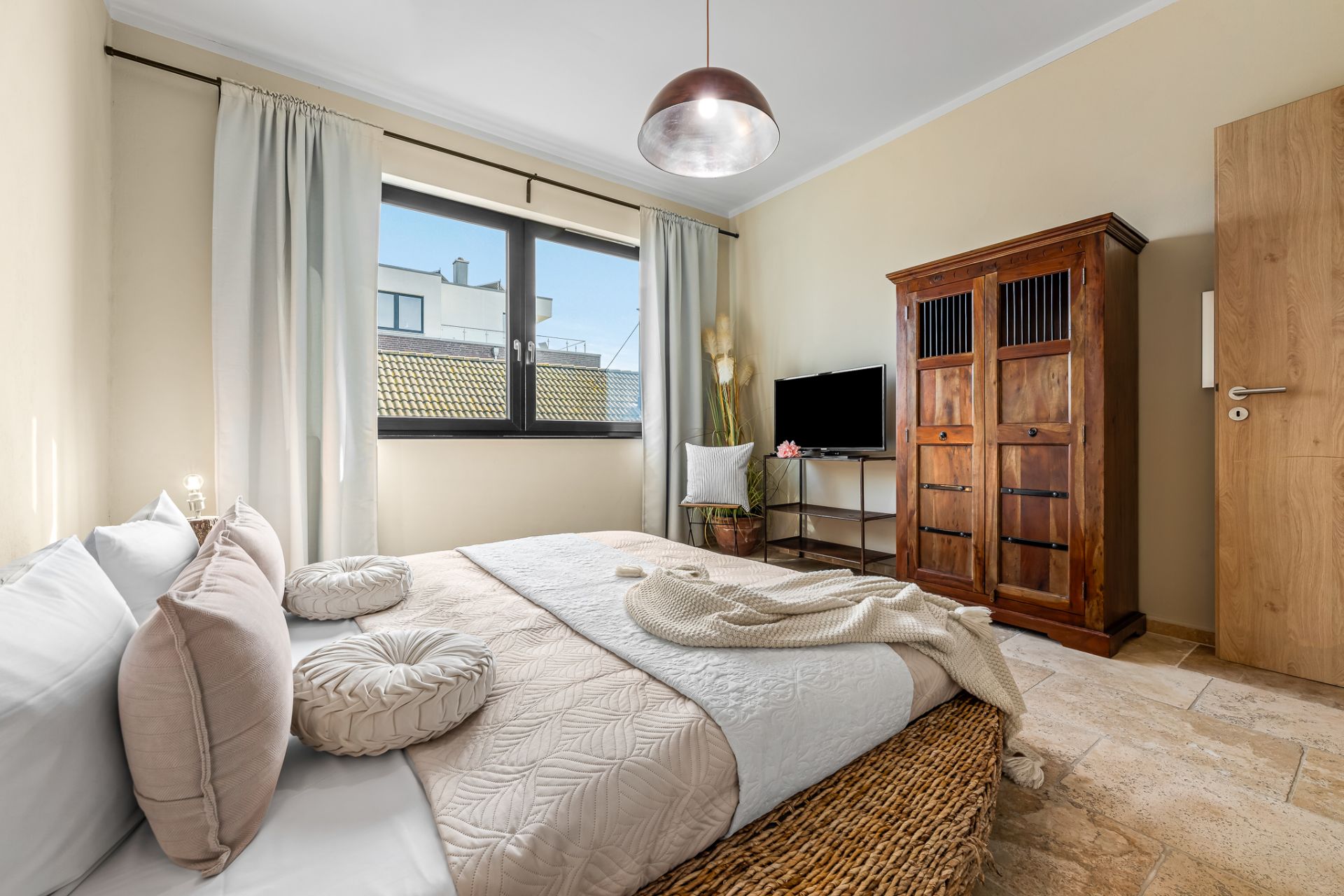 Helles Schlafzimmer mit Doppelbett, großem Fenster, Holzschrank, TV und Nachttisch.