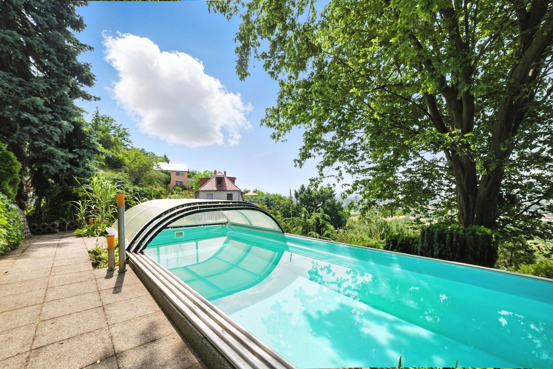 Außenpool mit Überdachung neben einem Gehweg und großen Bäumen im Garten.
