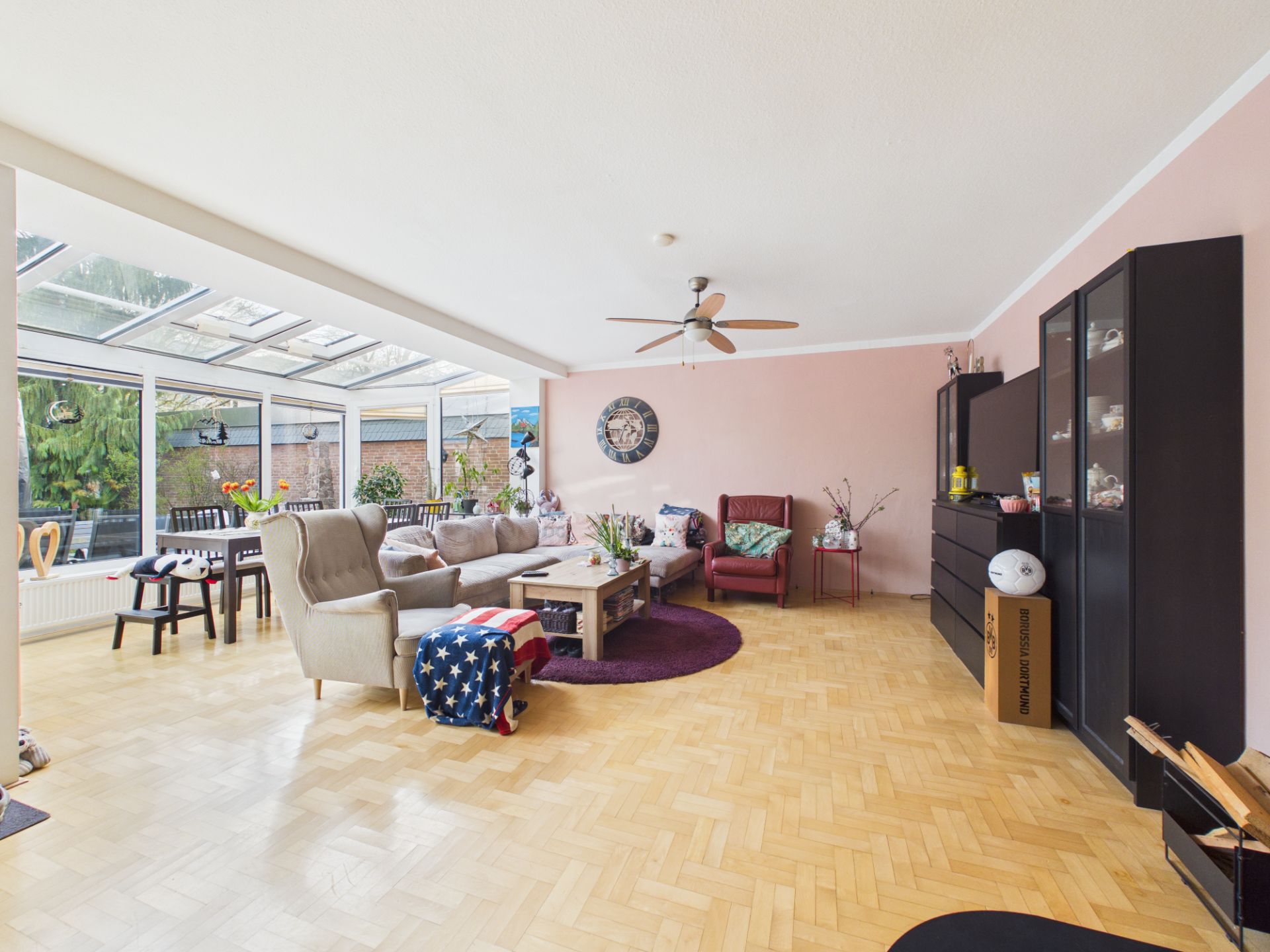 Helles Wohnzimmer mit Parkett, Glasdecke, Sofas, Sessel, Tisch und schwarzem Schrank.