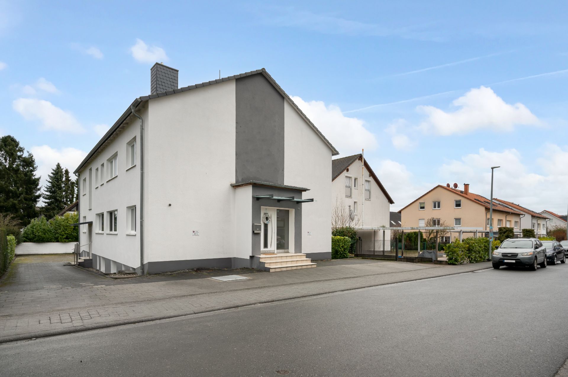 Zweistöckiges weißes Wohnhaus an einer ruhigen Straße mit geparkten Autos.