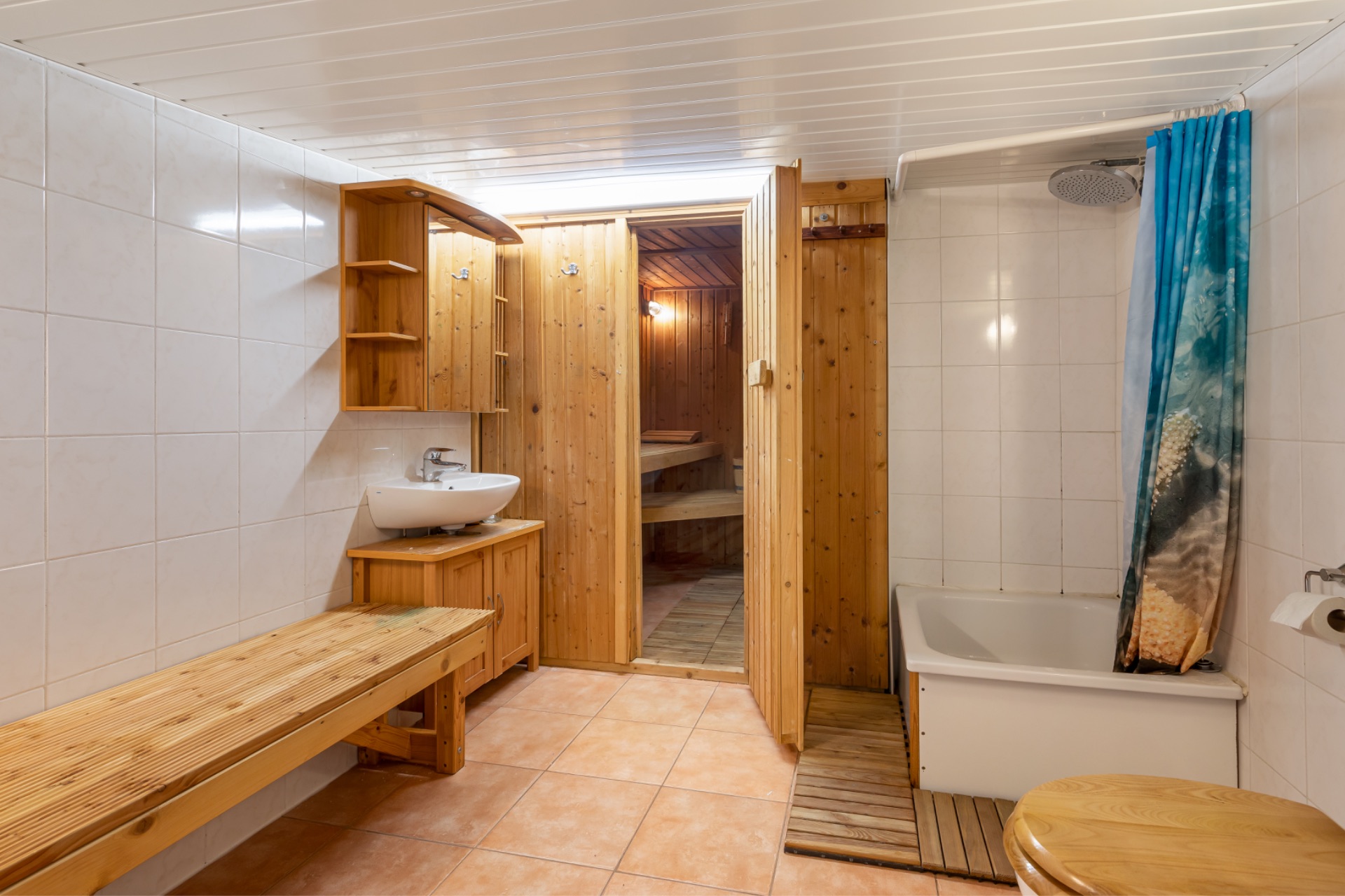 Badezimmer mit Holzsauna, Waschbecken, Dusche mit Duschvorhang und Holzbank.