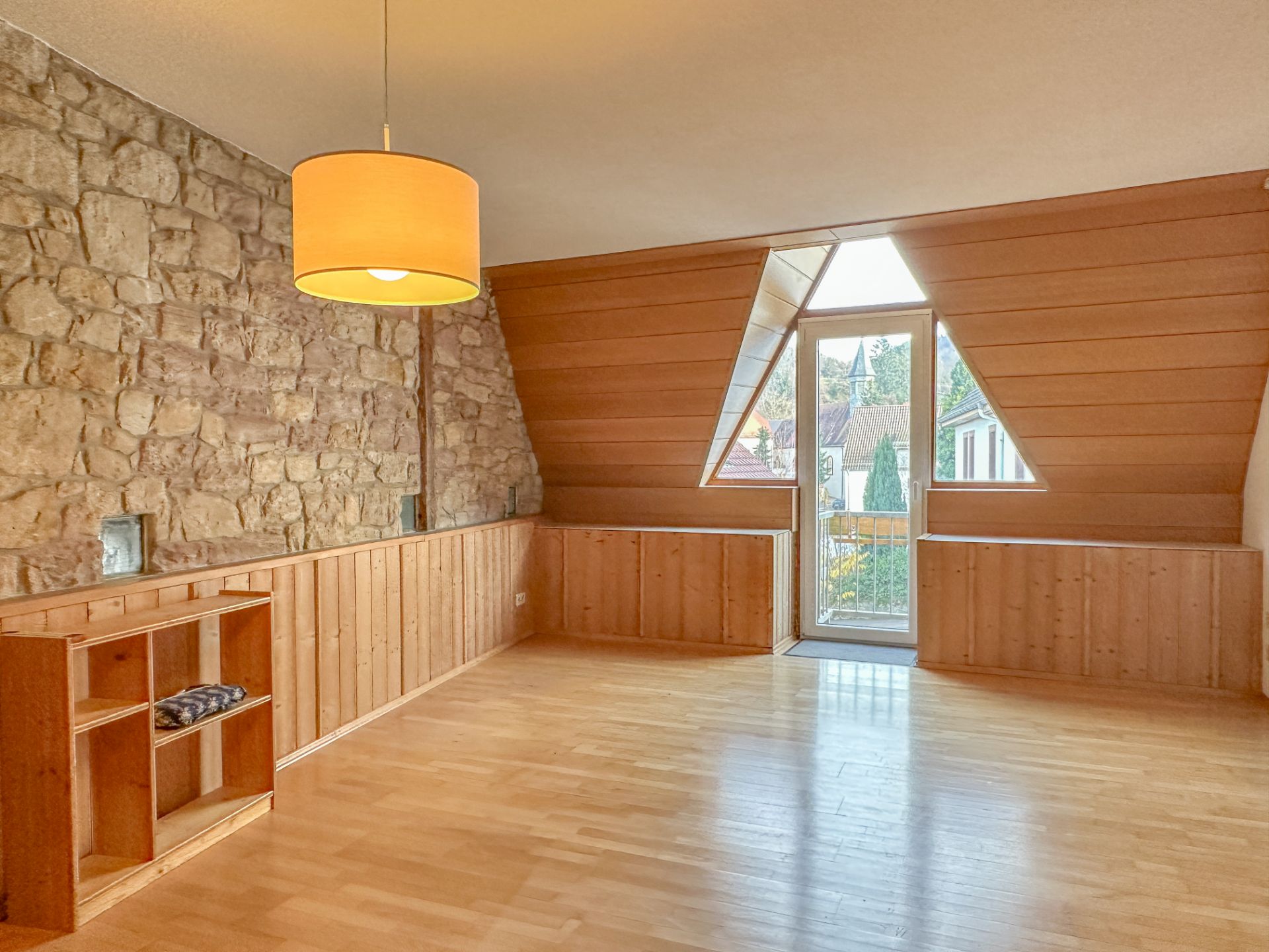 Wohnzimmer mit Stein- und Holzverkleidung, Holzregal und großer Fensterfront mit Tür zum Balkon.