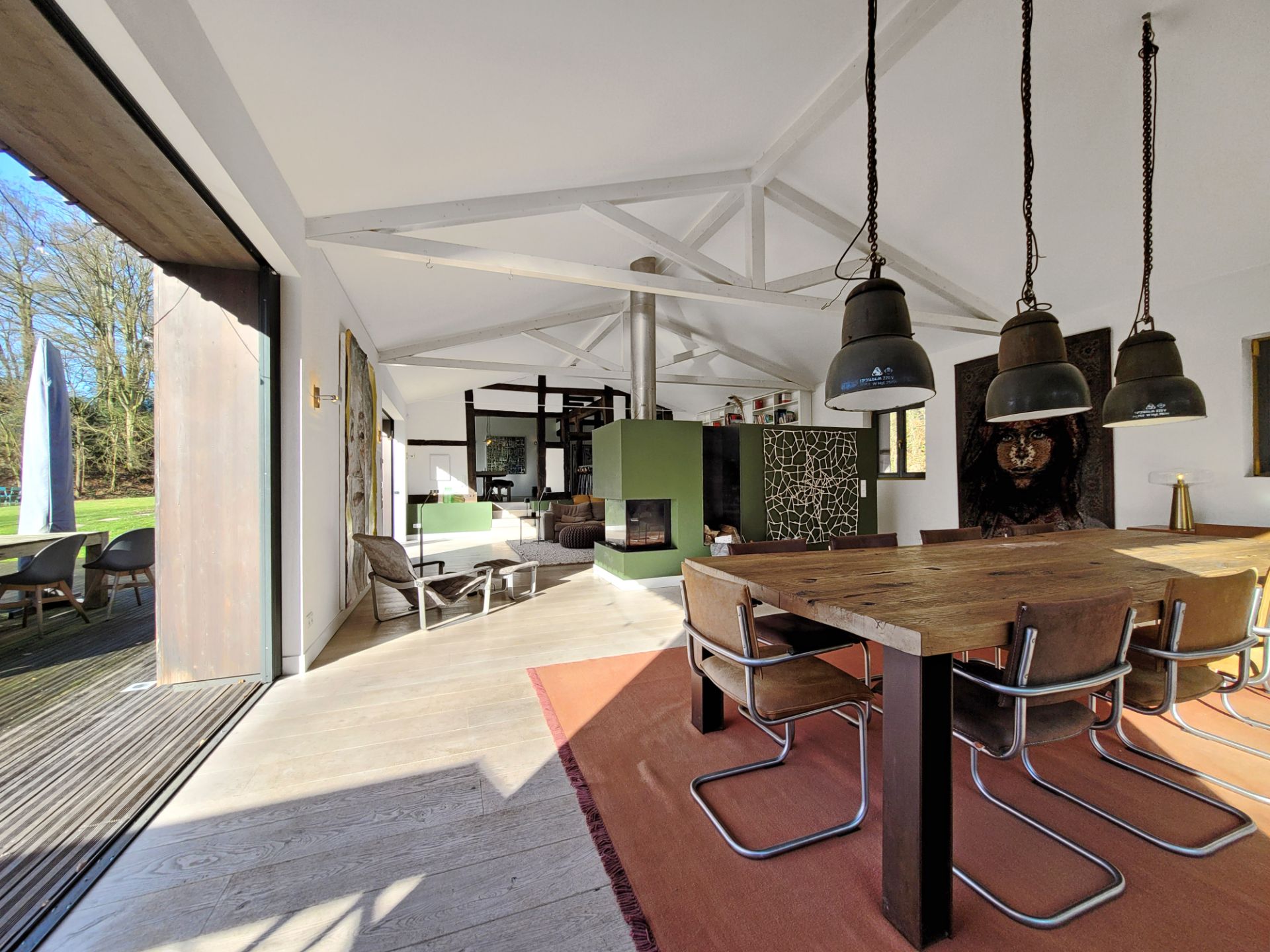 Helles Wohnzimmer mit Esstisch, offenen Türen zur Terrasse und sichtbaren Holzbalken.