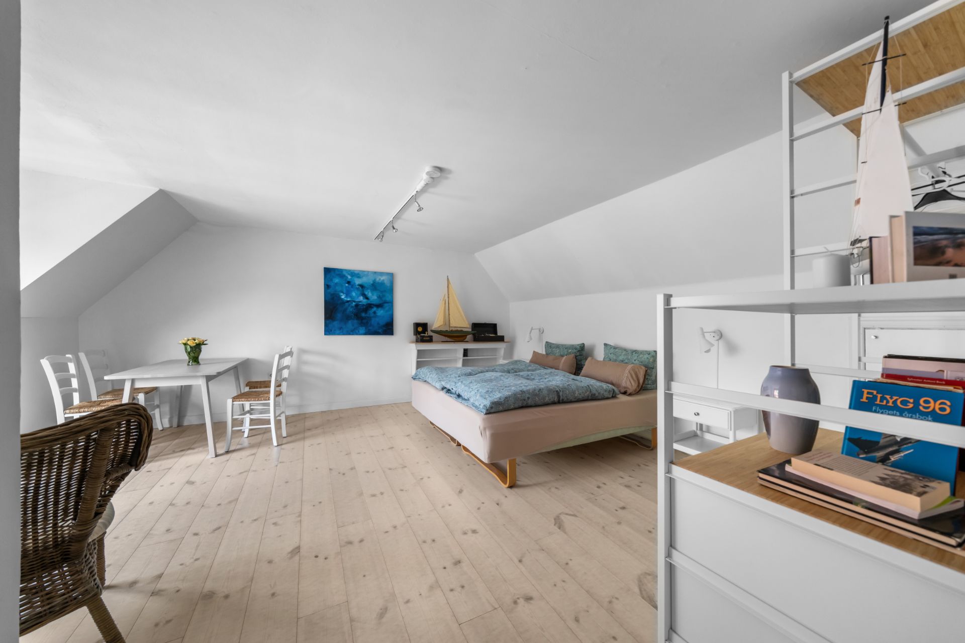 Helles Schlafzimmer mit Doppelbett, Esstisch, Stühlen und Regal auf hellem Holzboden.