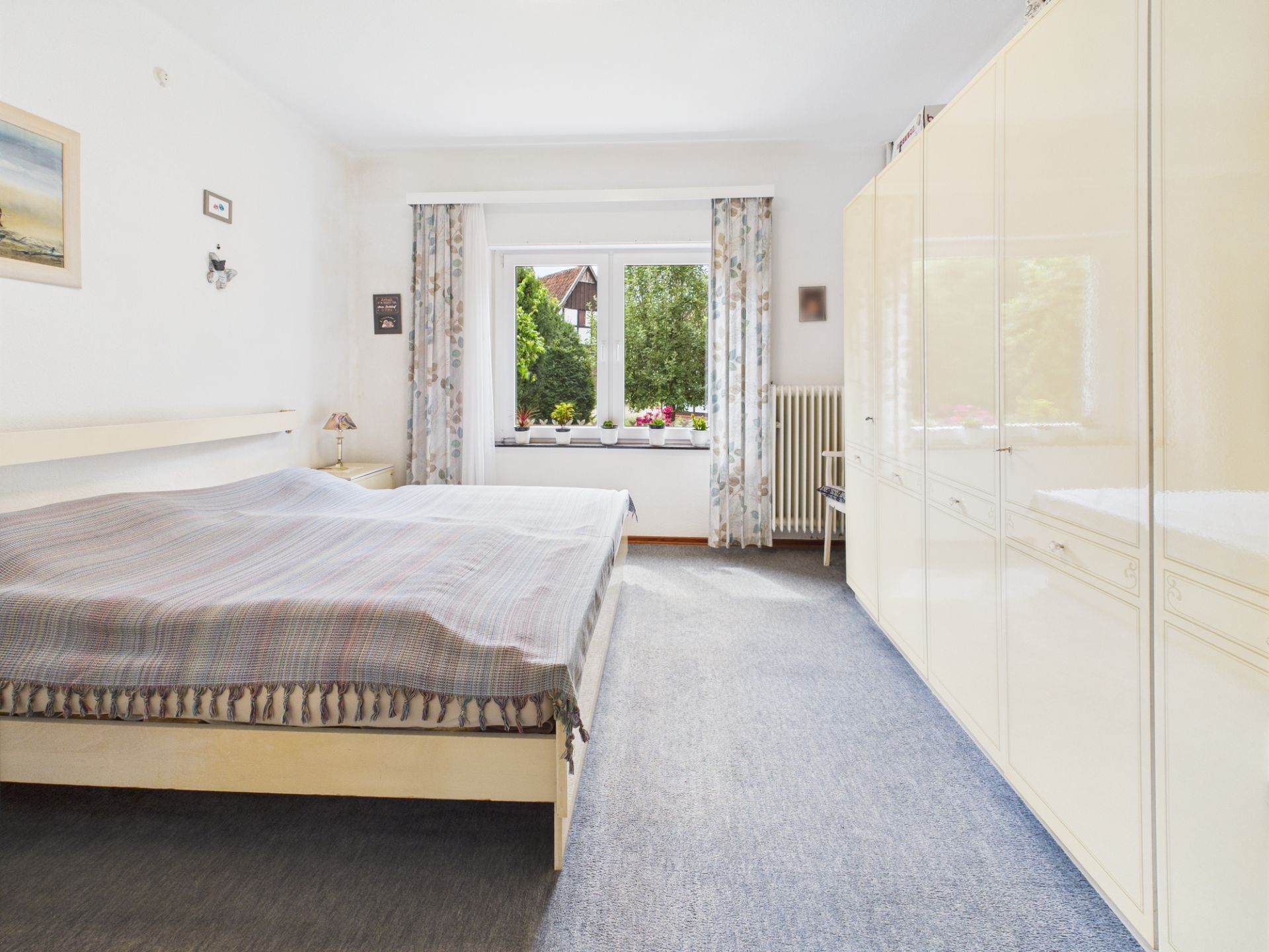 Helles Schlafzimmer mit Doppelbett, großem Kleiderschrank und Fenster mit Blick ins Grüne.