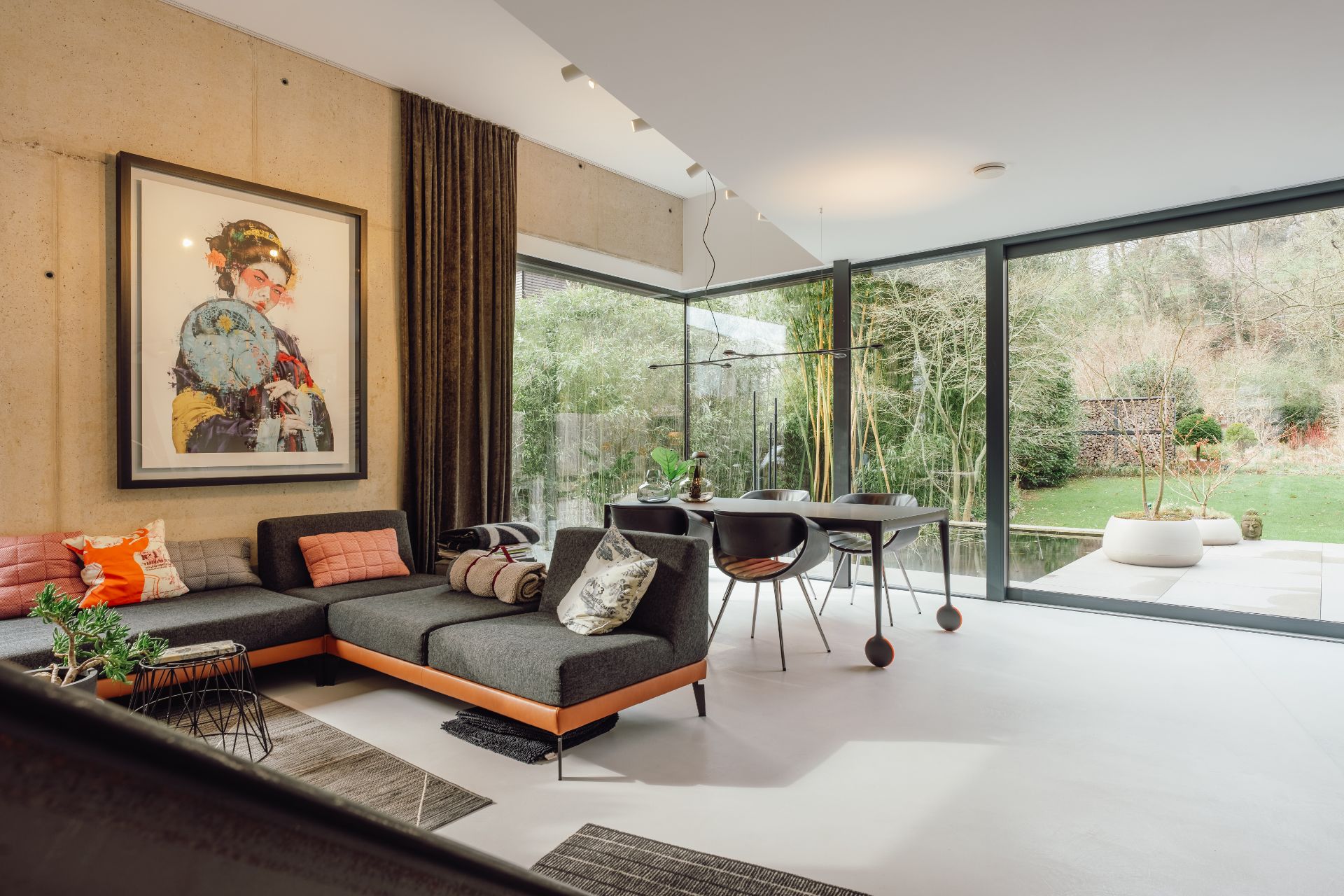 Modernes Wohnzimmer mit großer Glasfront, Sofa, Esstisch und Blick auf Garten.