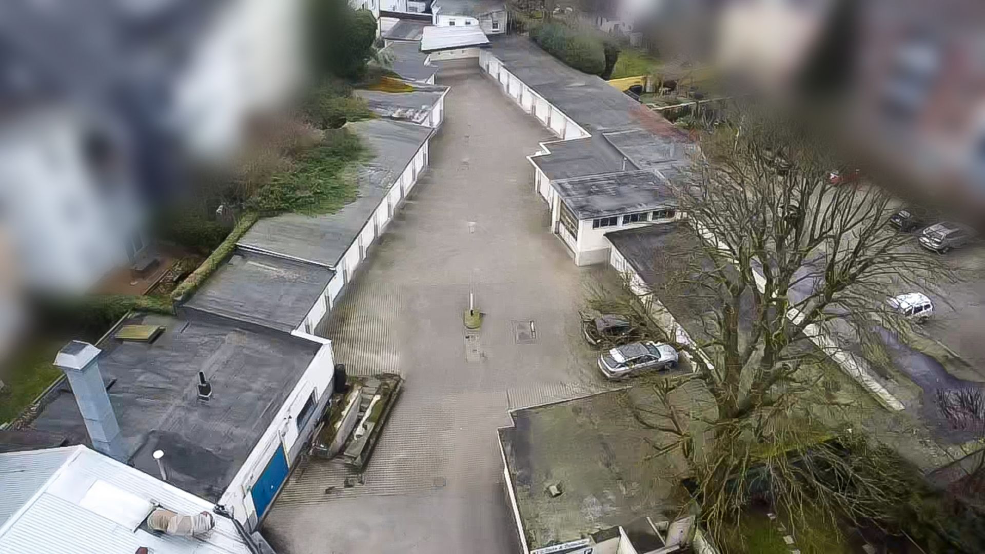 Luftaufnahme von mehreren Garagen und einem Innenhof mit einigen parkenden Autos und Bäumen.