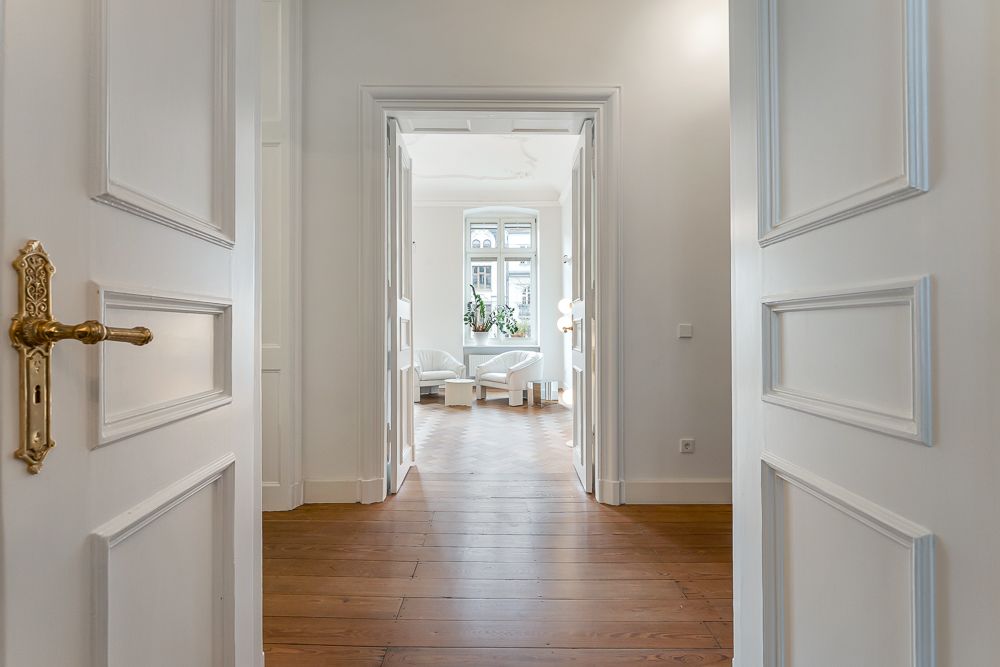 Heller Flur mit Holzboden, offener Tür und Blick ins Wohnzimmer mit Fenster und Sitzgruppe.