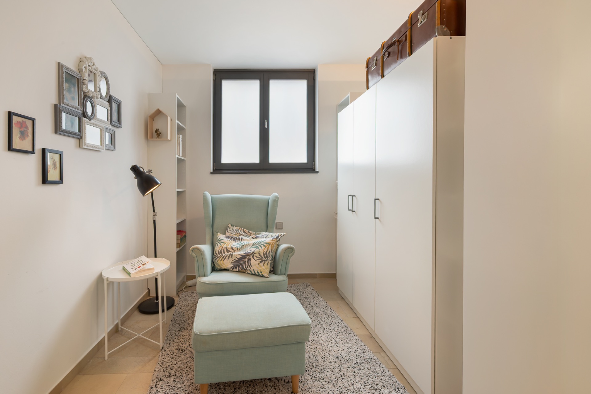 Heller Raum mit Sessel, Hocker, Teppich, Schrank und Fenster.