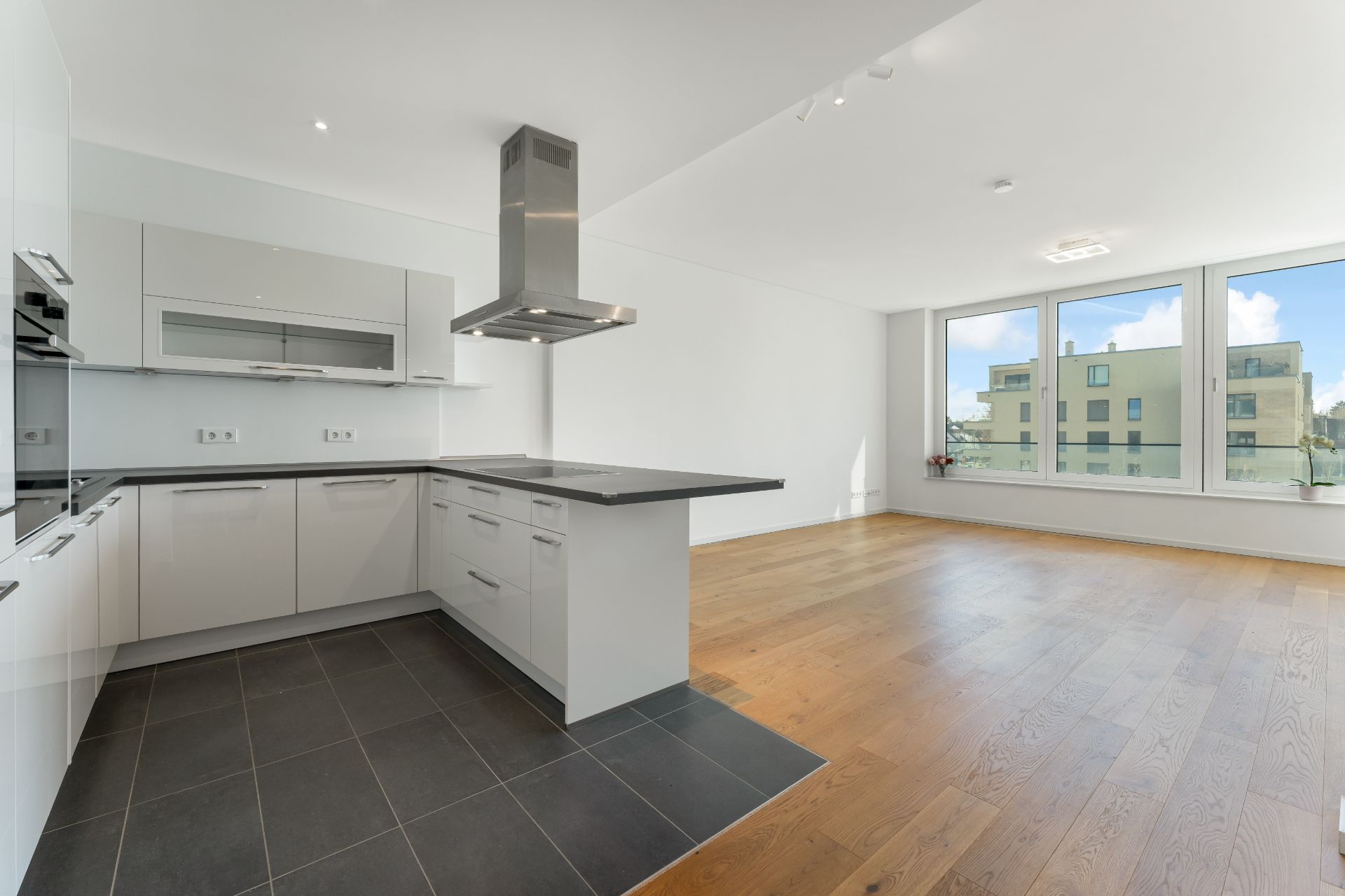 Moderne Einbauküche mit Kochinsel und offenem Wohnbereich, große Fenster mit Blick nach draußen.