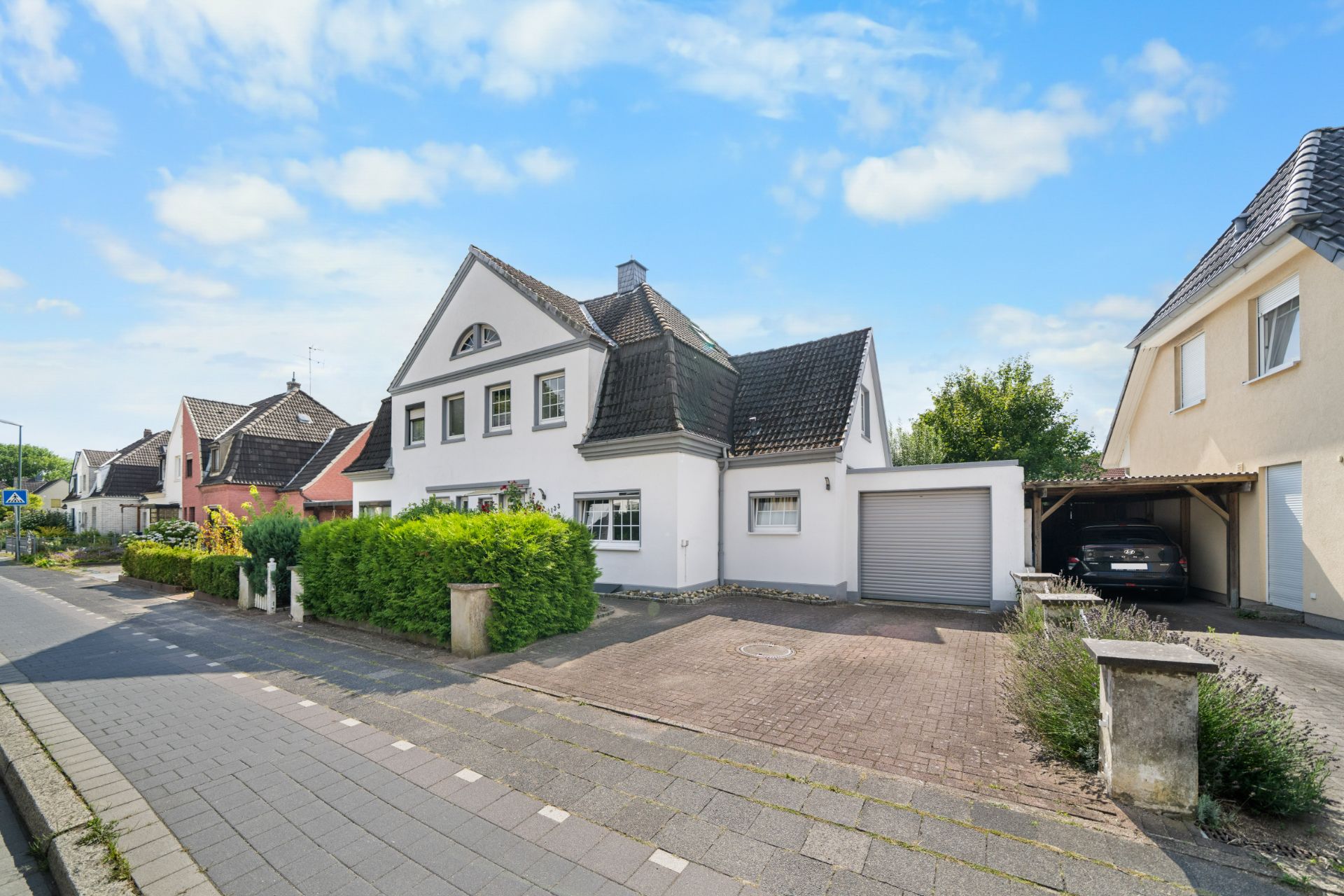 Weißes Einfamilienhaus mit Garage und gepflasterter Einfahrt in einer Wohnstraße.