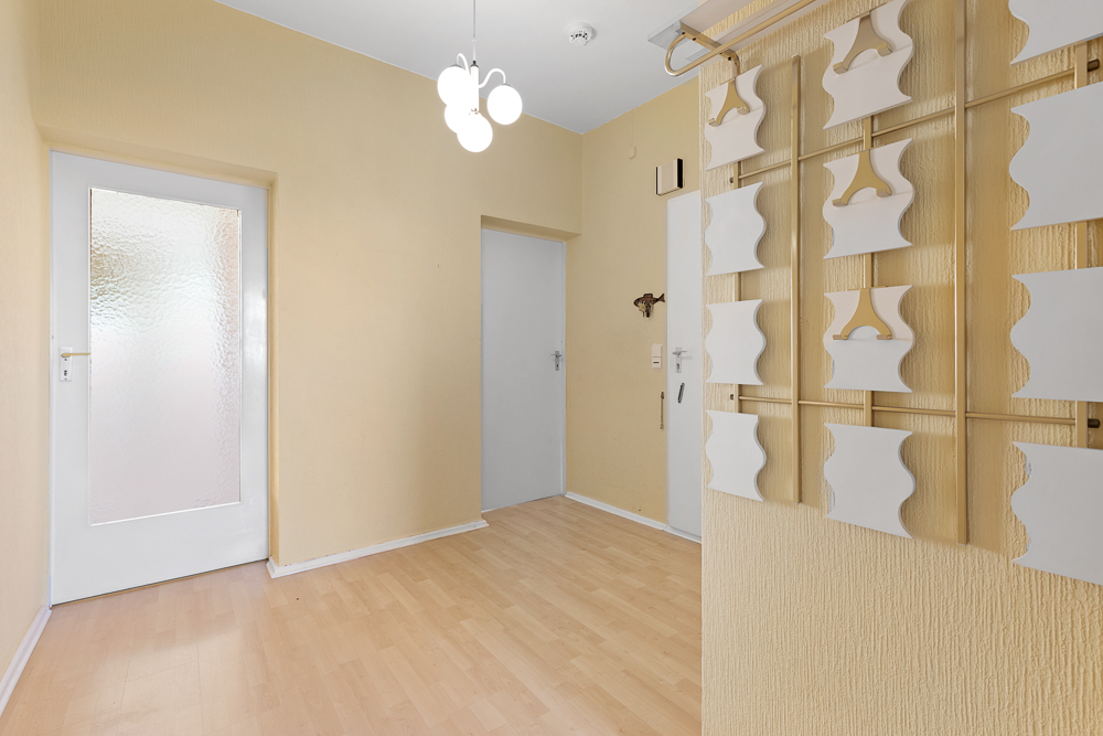 Heller Flur mit heller Holzboden, gelben Wänden und moderner Hänge-Dekoration an der Wand.