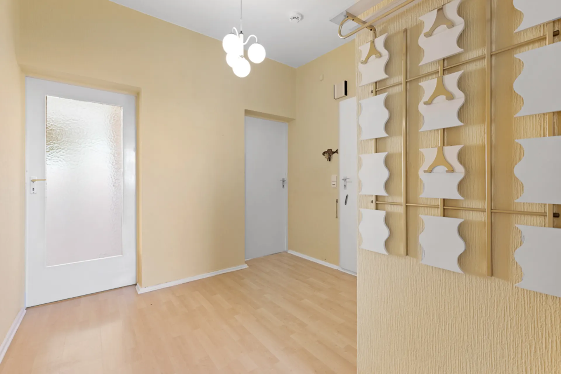 Heller Flur mit heller Holzboden, gelben Wänden und moderner Hänge-Dekoration an der Wand.