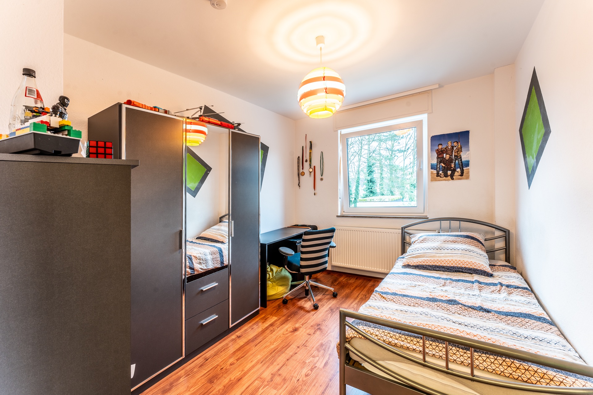 Helles Jugendzimmer mit Einzelbett, Schreibtisch, Kleiderschrank und Fenster mit Blick ins Grüne.