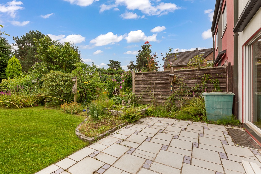 Gepflasterte Terrasse mit Blick auf einen gepflegten Garten und eine Holzzaunabgrenzung.