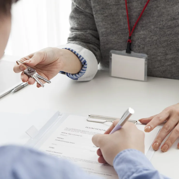 Eine Person übergibt einen Schlüsselbund, während eine andere ein Formular unterschreibt.