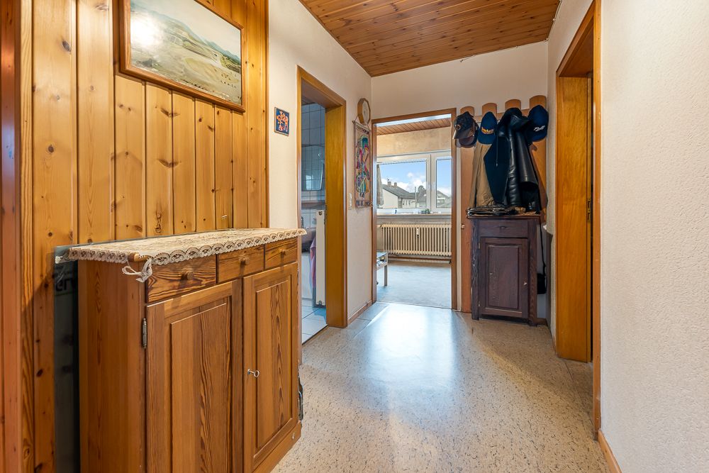 Flur mit Holzverkleidung, Garderobe, Schrank und Blick in ein Zimmer mit Fenster.