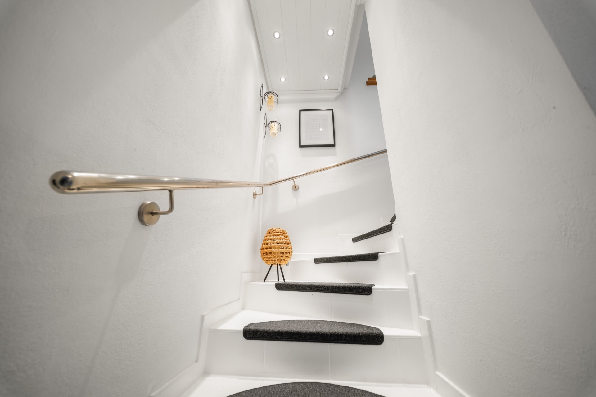 Weiße Treppe mit schwarzem Teppich, Wandbild, Lampen und Handlauf in einem Wohnhaus.