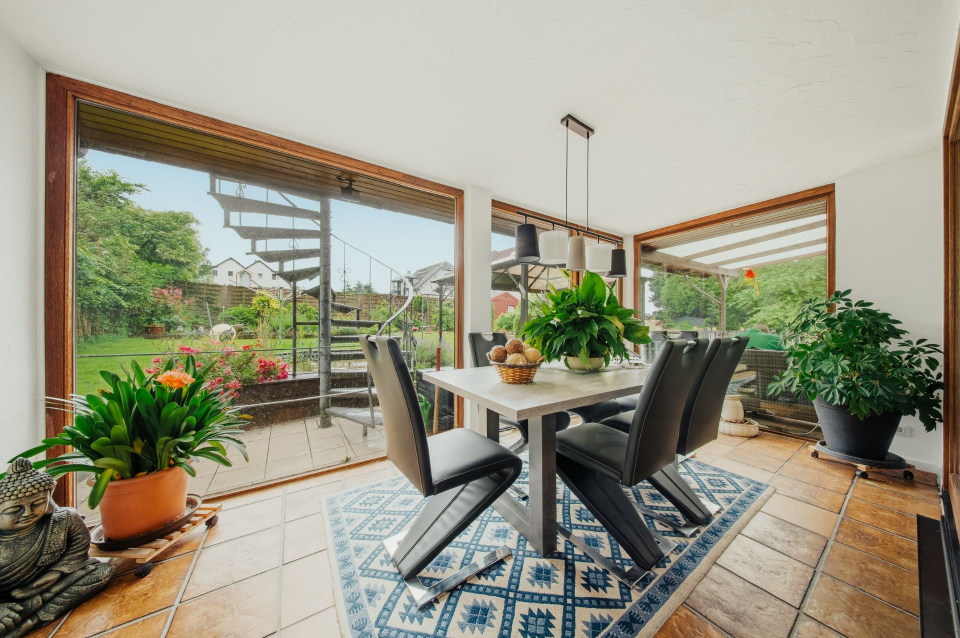 Heller Essbereich mit sechs Stühlen, großen Fenstern, Pflanzen und Blick in den Garten mit Wendeltreppe.