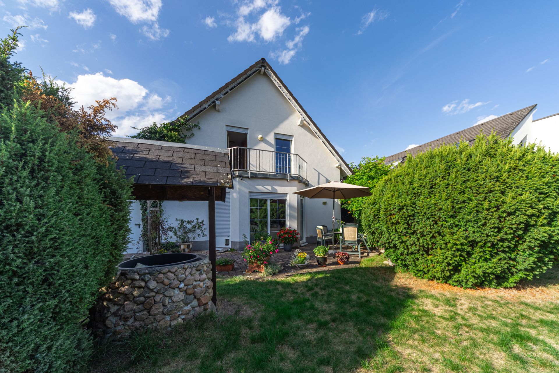 Garten mit Terrasse, Sitzgruppe und Sonnenschirm vor einem weißen Einfamilienhaus.