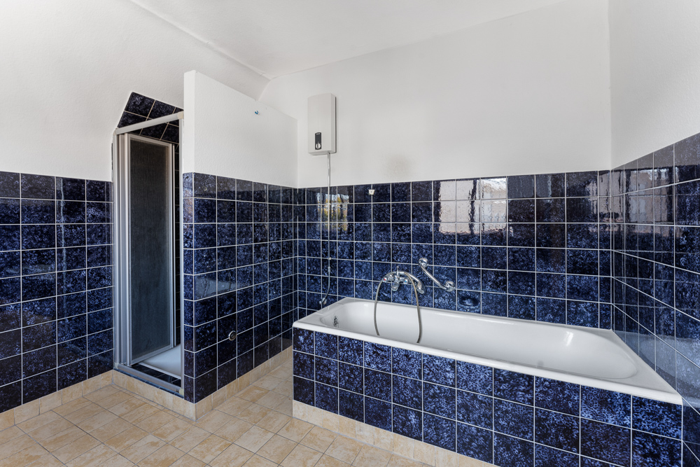 Ein Badezimmer mit blauen Fliesen, Badewanne und abgetrennter Dusche ist sichtbar.