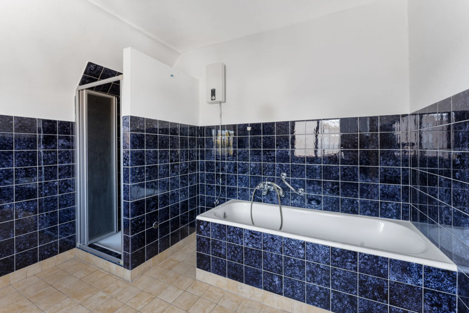Ein Badezimmer mit blauen Fliesen, Badewanne und abgetrennter Dusche ist sichtbar.