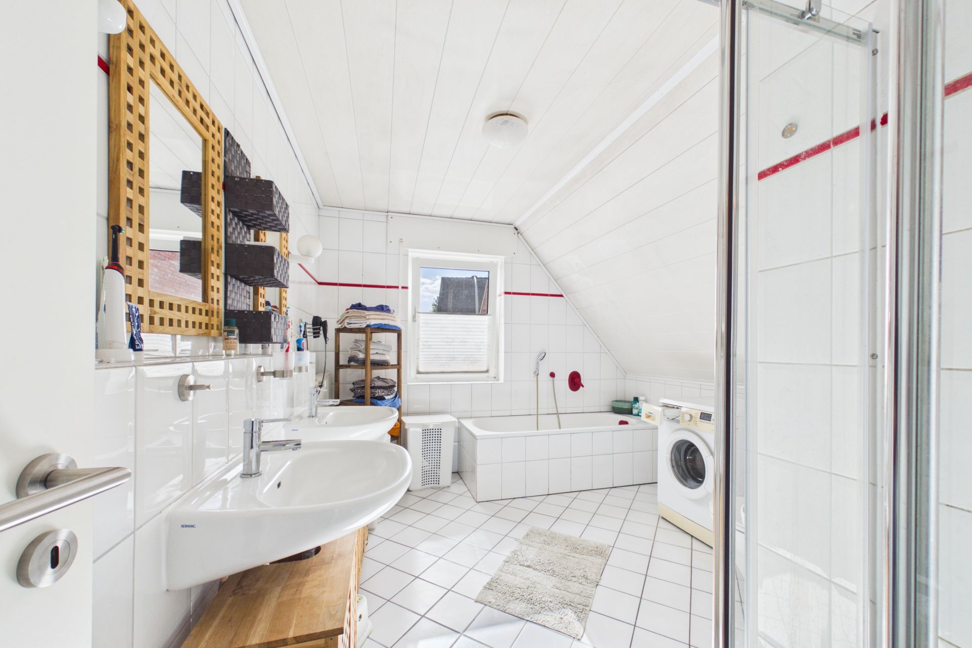 Helles Badezimmer mit zwei Waschbecken, Badewanne, Dusche und Waschmaschine unter schräger Decke.