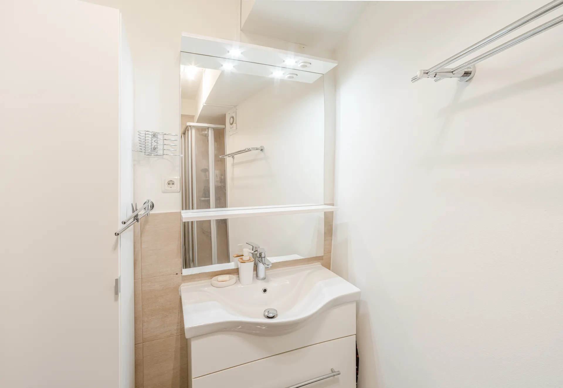 Helles Badezimmer mit Waschbecken, großem Spiegel und Handtuchhalter an der Wand.