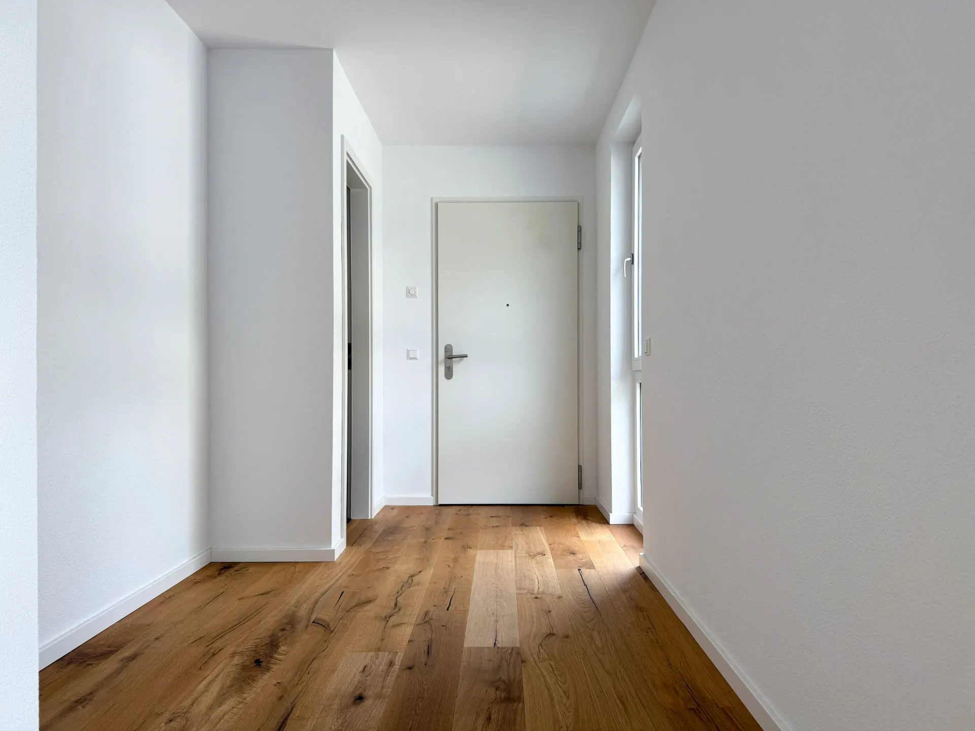 Heller Flur mit Holzboden, weißer Wand und weißer Eingangstür.