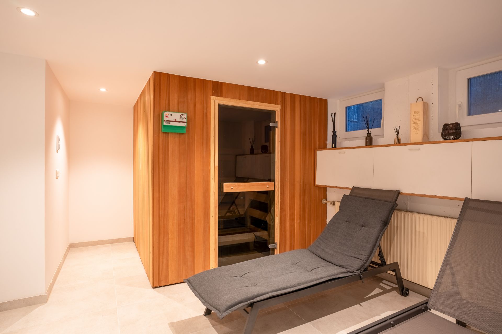 Heller Raum mit Holzsauna, Liegestuhl und weißen Hängeschränken an der Wand.