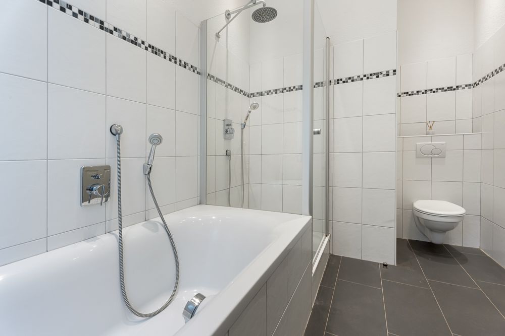 Modernes Badezimmer mit Badewanne, Dusche und Toilette, weiße Fliesen an den Wänden.