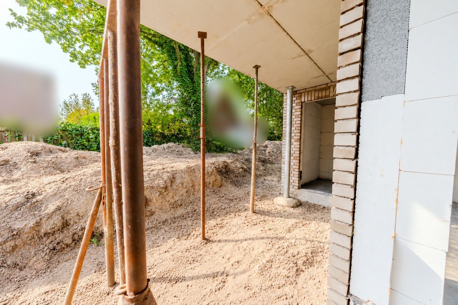 Eine Baustelle mit offener Wand, Baustützen und Erdhaufen im Hintergrund.