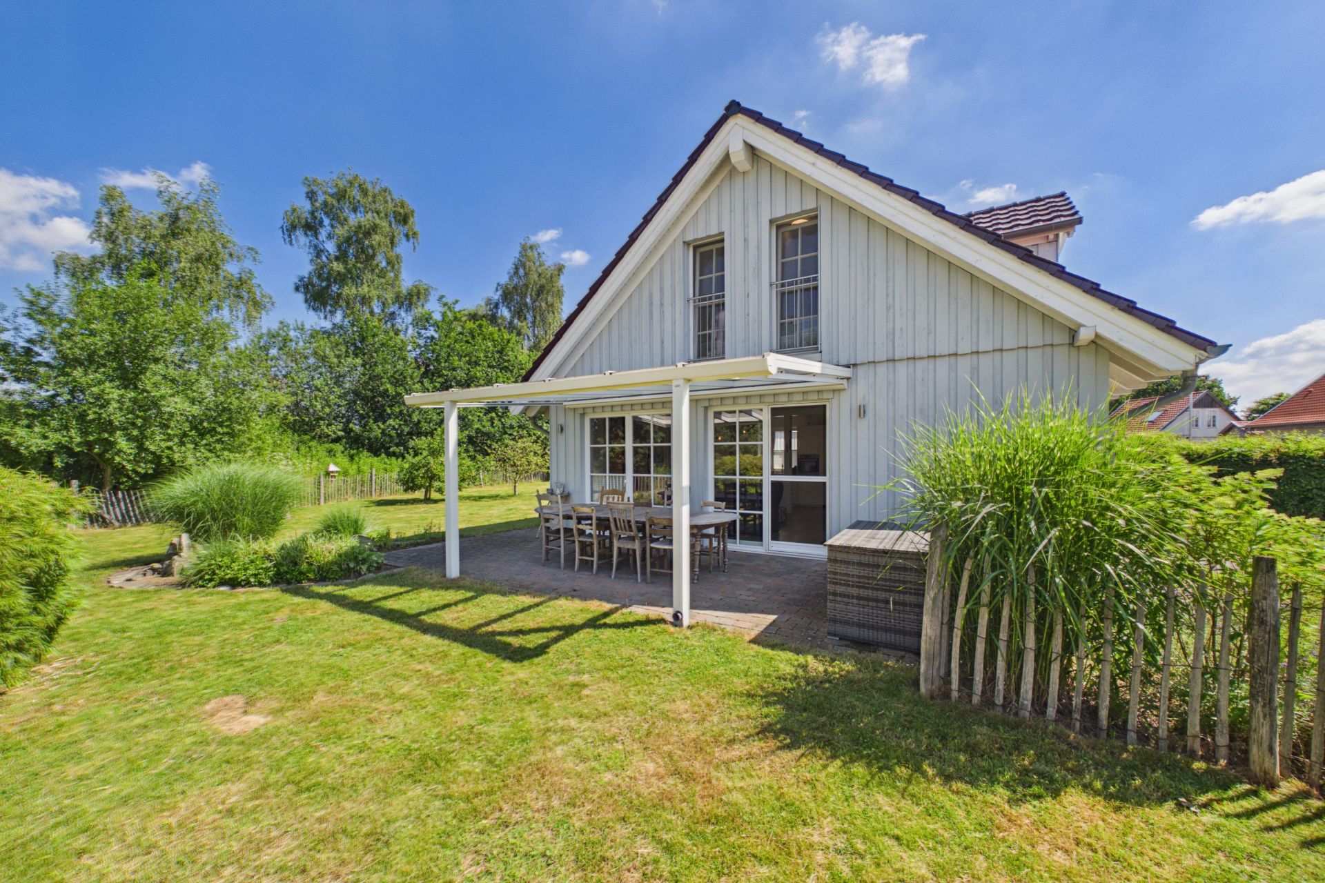 Haus mit Terrasse, Gartenmöbeln und großem Garten, umgeben von Bäumen und Gras.