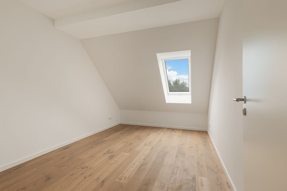 Leeres Zimmer mit schräger Decke, Dachfenster und Holzfußboden.