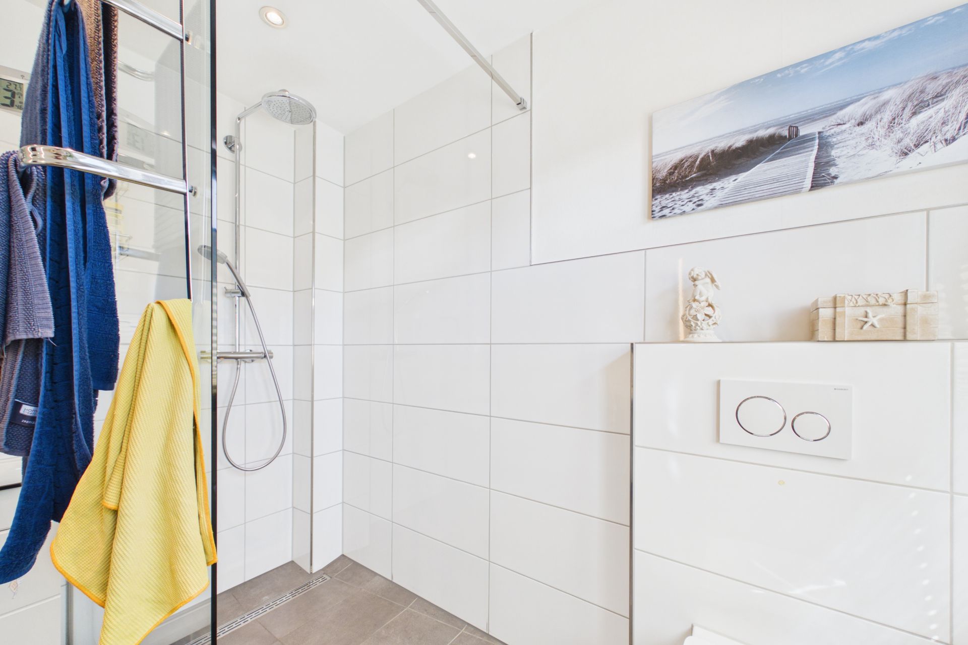 Helles Badezimmer mit Dusche, Handtüchern, WC und Wandbild.