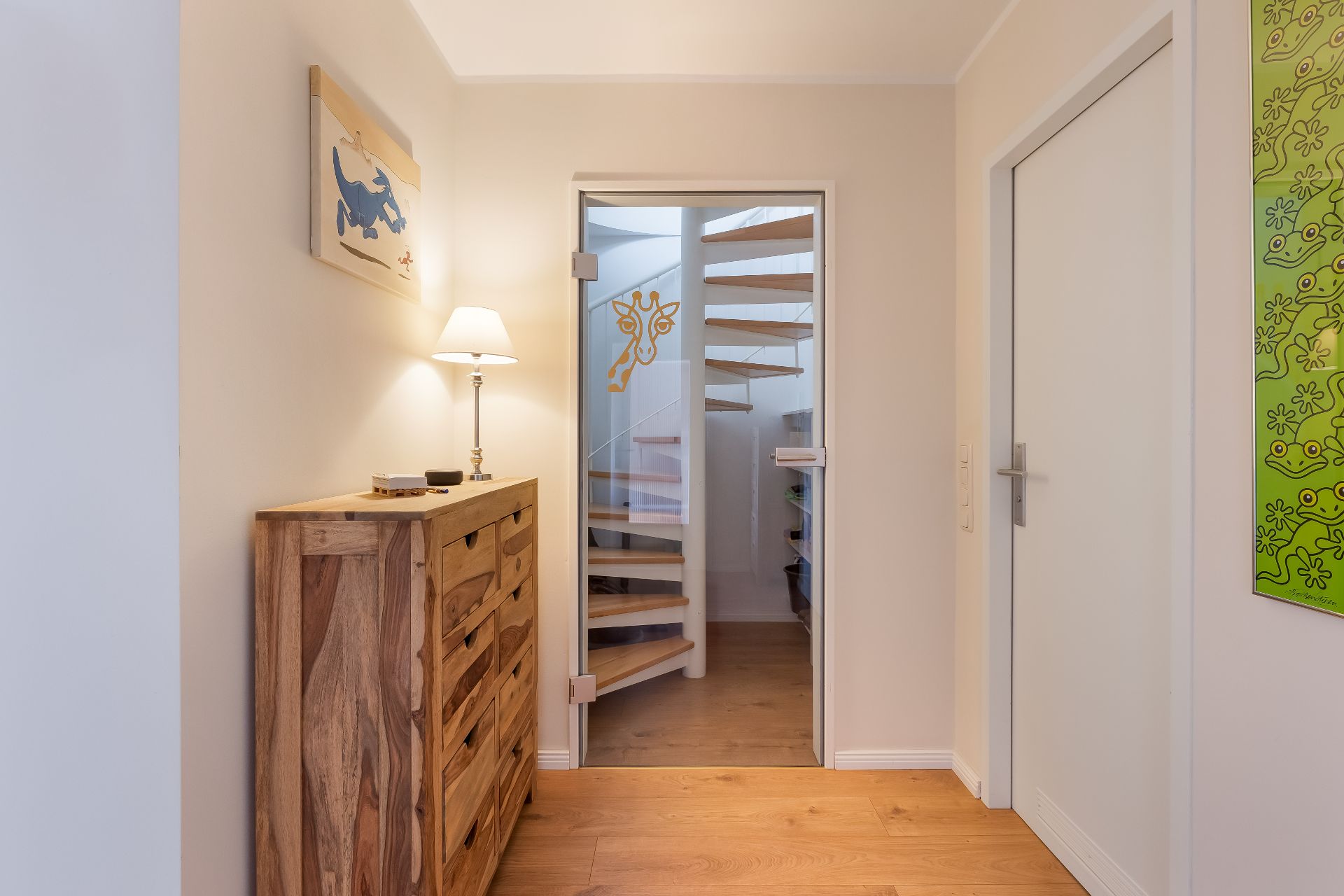 Heller Flur mit Holzkommode, Lampe und Glastür zu einer Wendeltreppe.