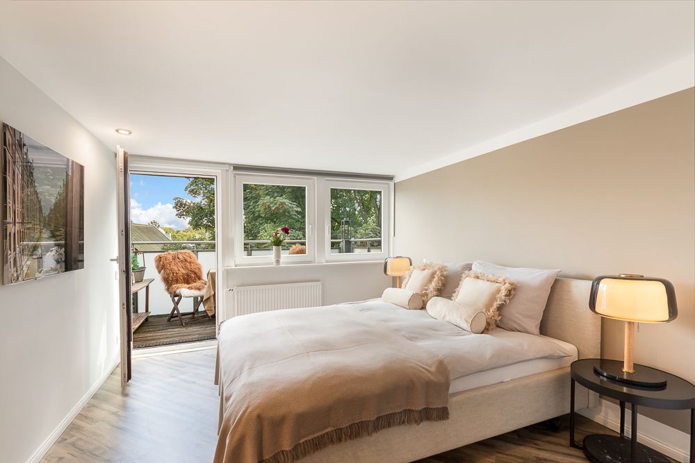 Helles Schlafzimmer mit Doppelbett, zwei Nachttischen und Zugang zu einem Balkon mit Stuhl.