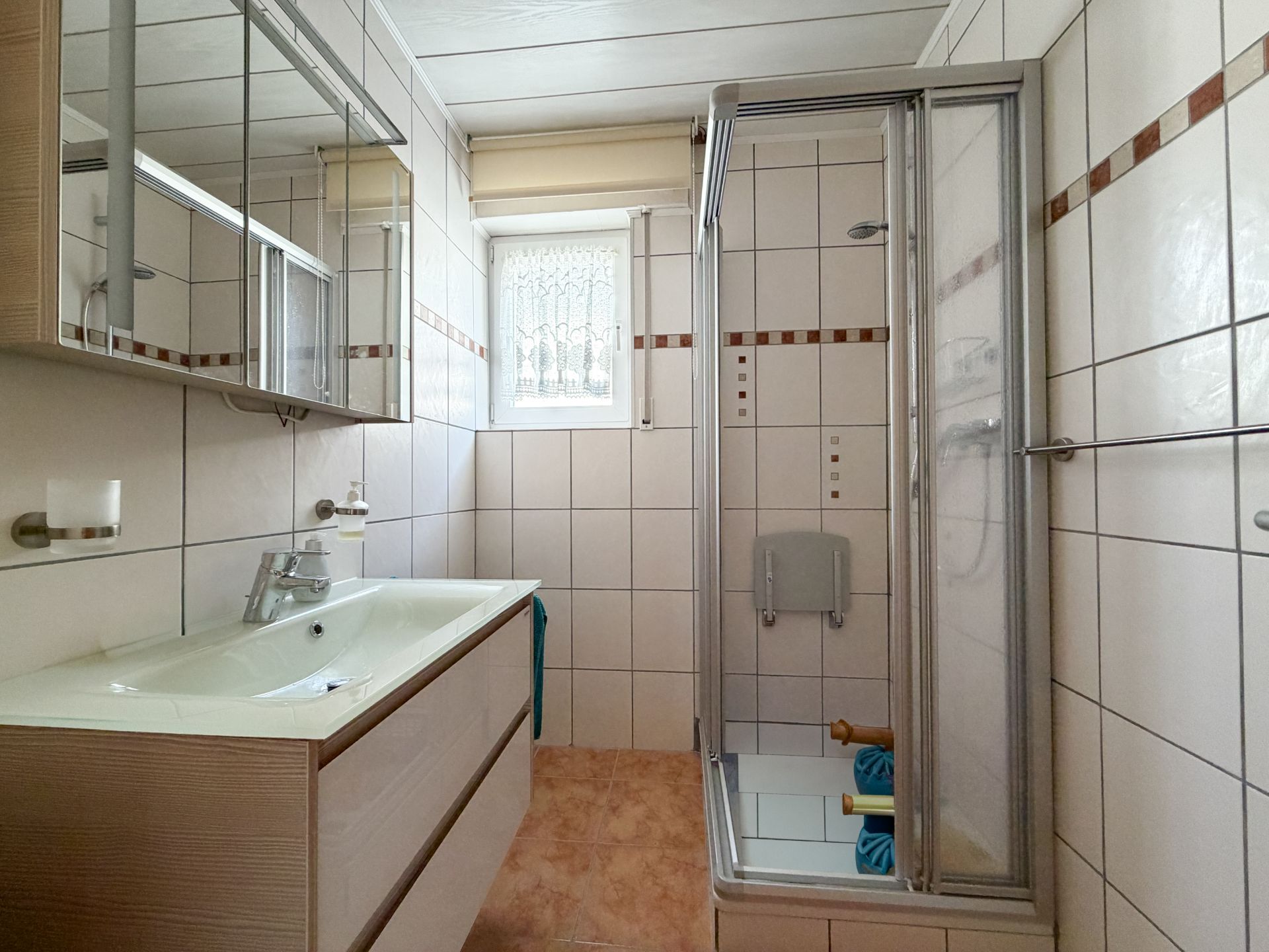 Modernes Badezimmer mit Waschbecken, Spiegel, Dusche und Fenster mit Gitter.