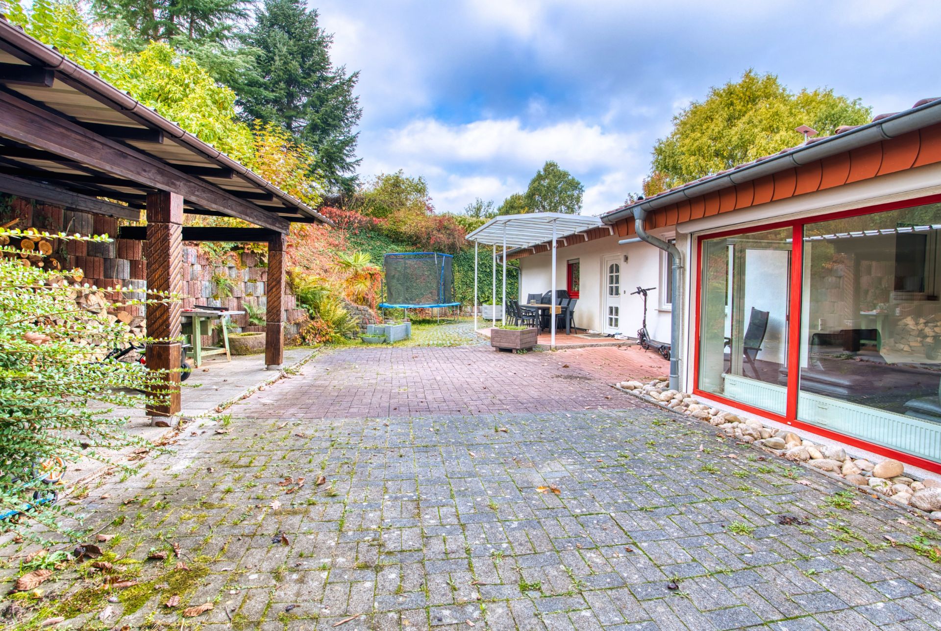 Gepflasterter Innenhof mit überdachtem Sitzbereich und großem Fenster an einem Wohnhaus.