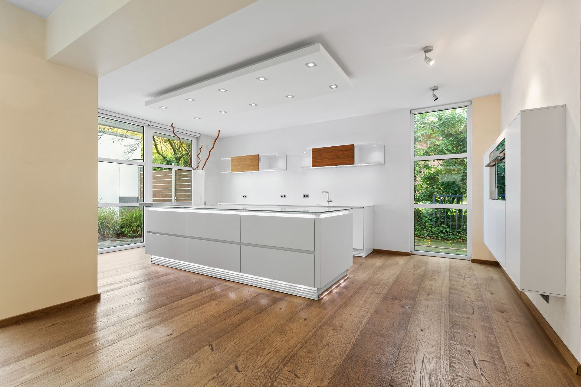 Moderne, helle Küche mit Holzfußboden und großen Fenstern mit Blick ins Grüne.