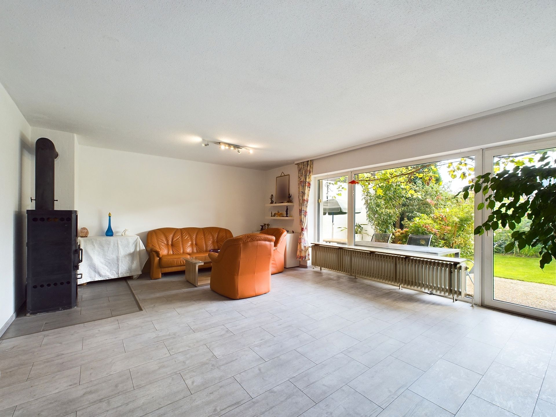 Helles Wohnzimmer mit Kaminofen, Ledersofas und großen Fenstern mit Blick in den Garten.