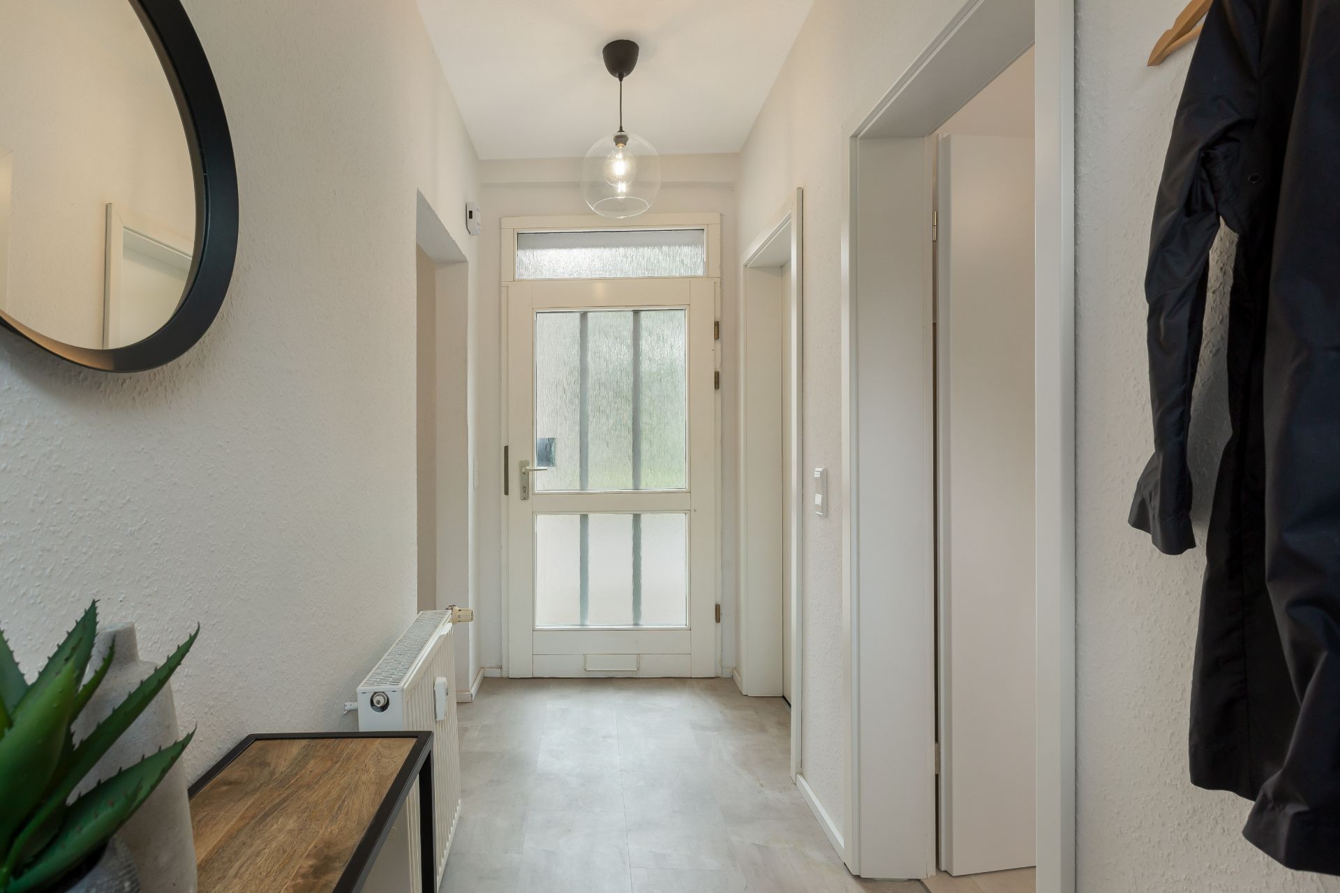 Heller Flur mit weißer Haustür, Spiegel, Tisch und einer hängenden Jacke an der Wand.