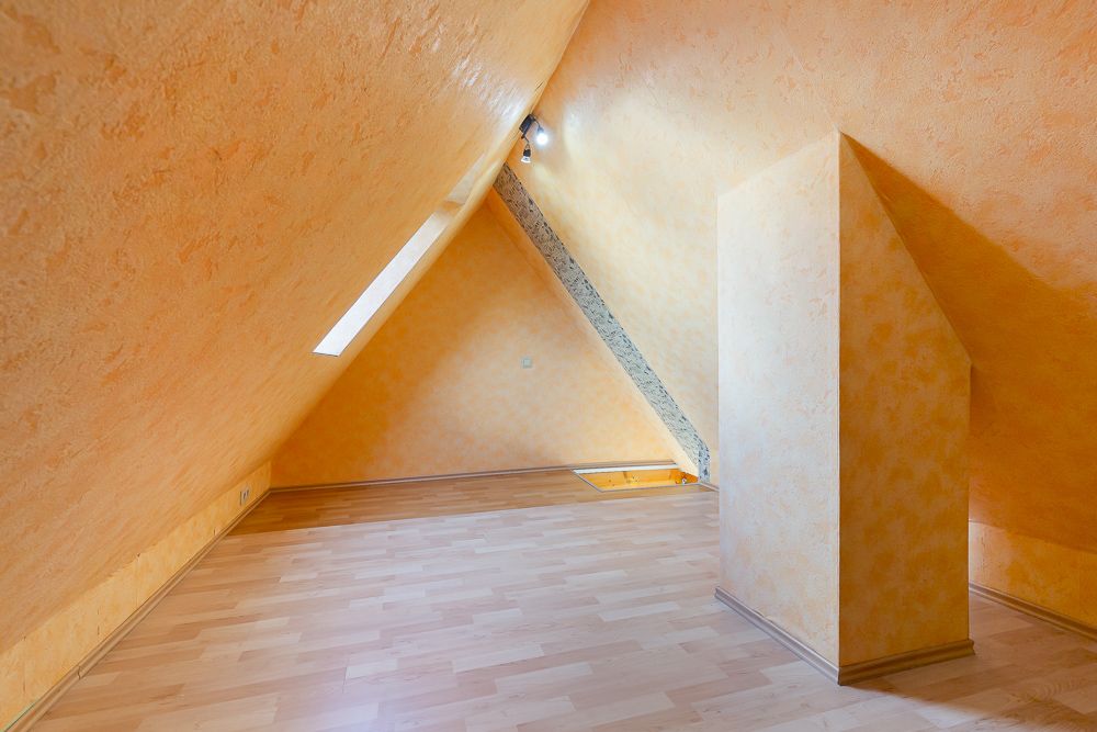 Dachgeschossraum mit schrägen Wänden, gelben Wänden und Laminatboden.