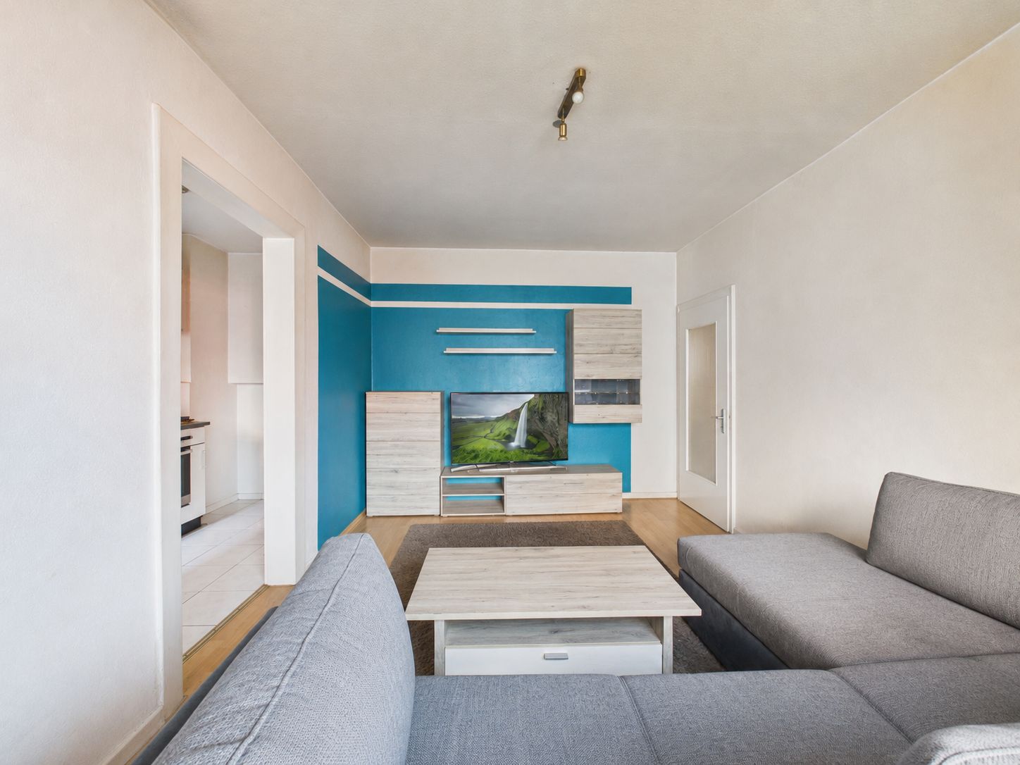 Modernes Wohnzimmer mit grauem Sofa, Couchtisch und TV-Wand mit blauer Akzentwand.
