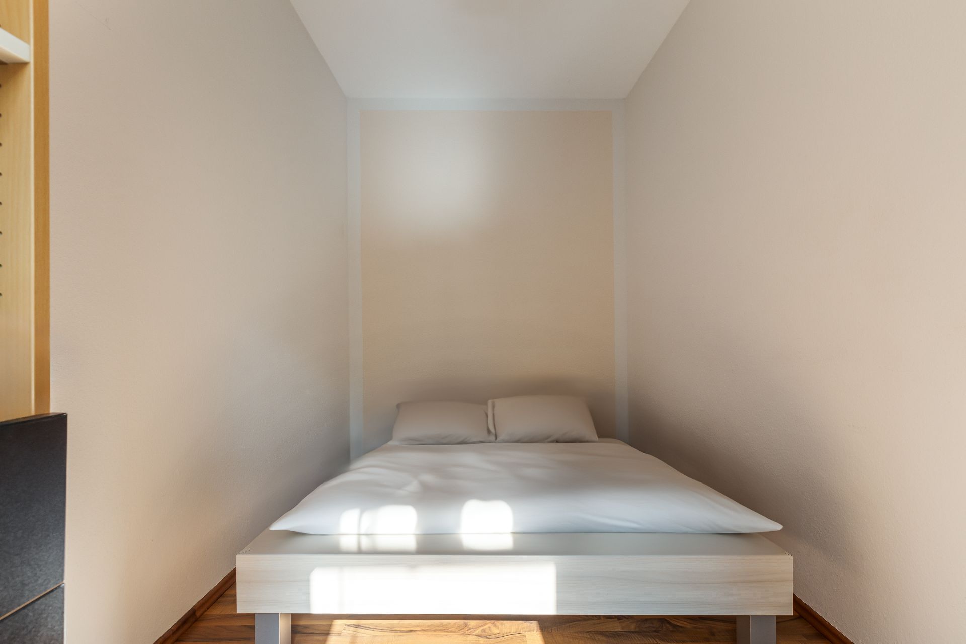 Kleines Schlafzimmer mit einem Doppelbett und weißen Bettwaren, umgeben von hellen Wänden.