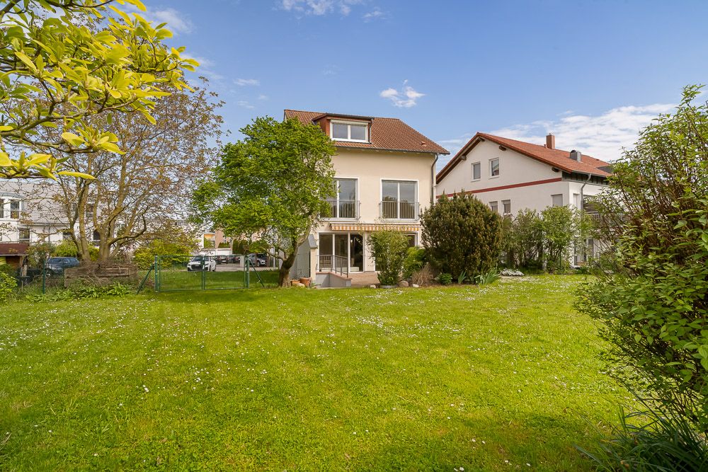 Zweistöckiges Wohnhaus mit Garten, umgeben von Bäumen und Wiese, bei klarem Himmel.