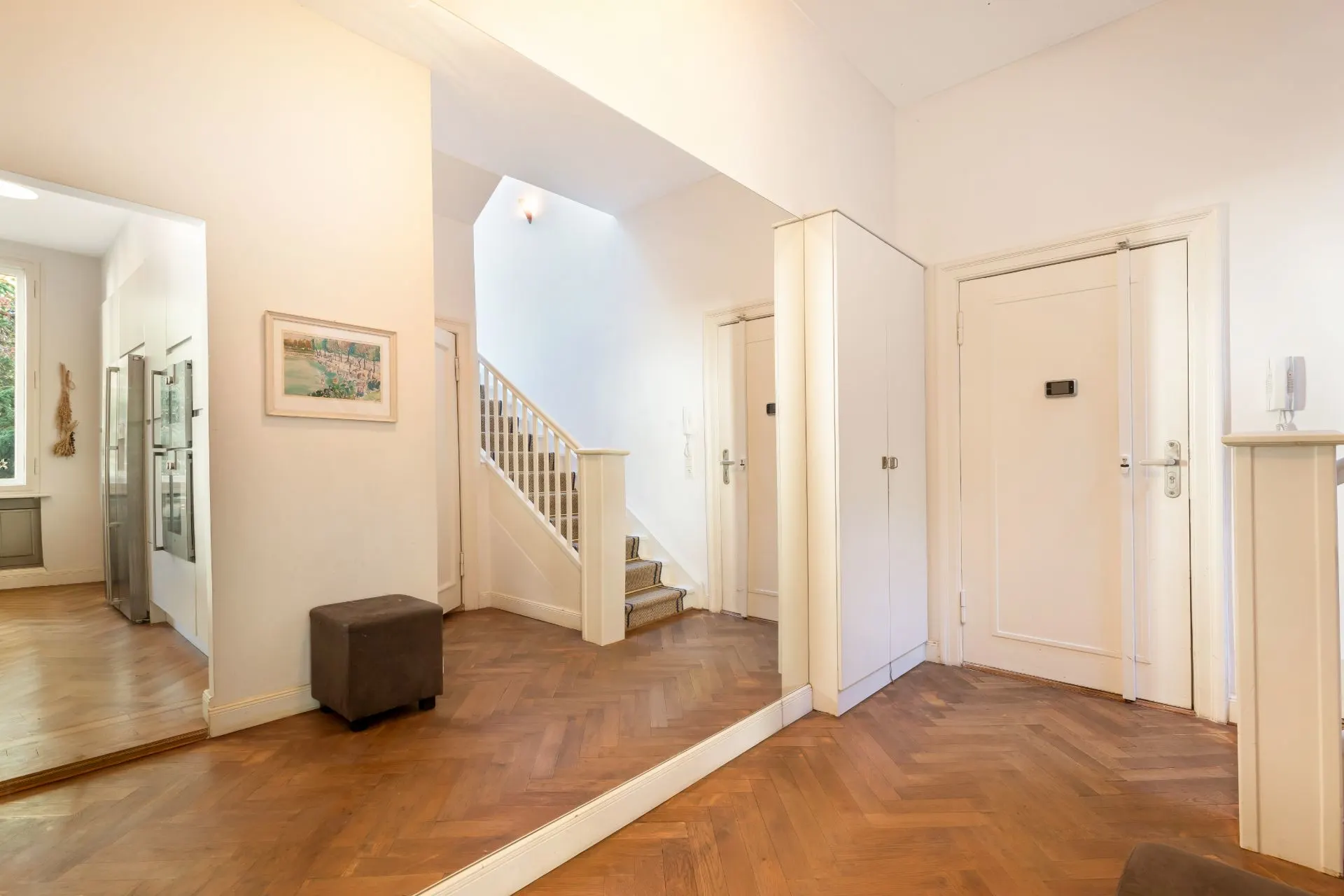 Heller Flur mit Spiegel, Holzboden, Treppe, Türen und Hocker.